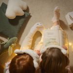 Two children in pajamas reading a book together at bedtime with soft lighting and toys around.